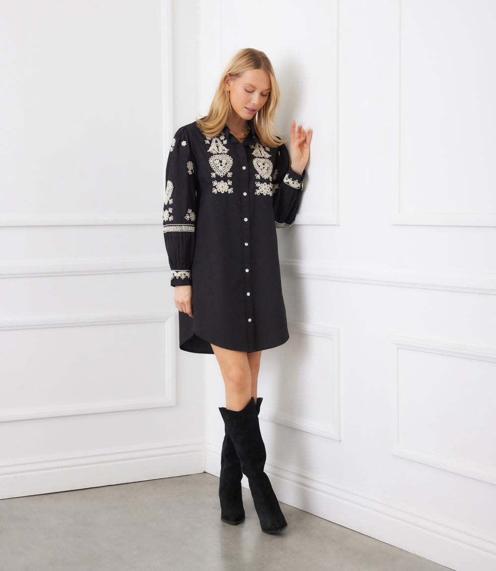 Woman wearing black blouson sleeve shirtdress with cream rope-stitch embroidery and shell buttons