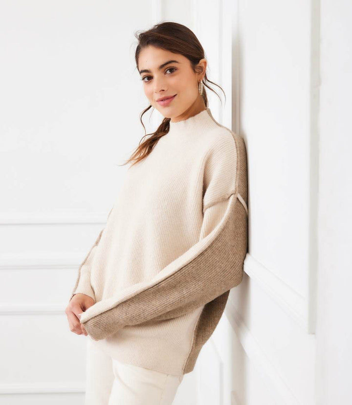 Woman wearing beige and brown colorblock mock neck sweater with drop shoulder sleeves and relaxed fit standing indoors