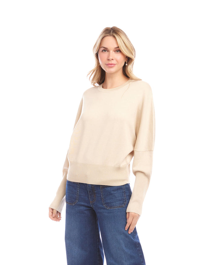 Woman wearing beige dolman sleeve sweater with crew neck and ribbed cuffs paired with blue jeans