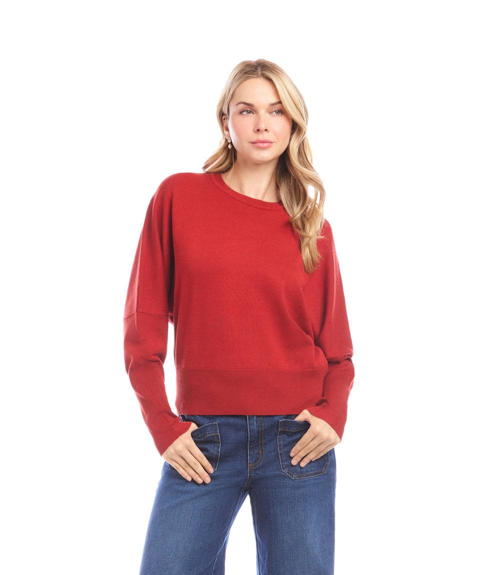 Woman wearing a red dolman sleeve sweater with tapered sleeves and crew neckline paired with blue jeans