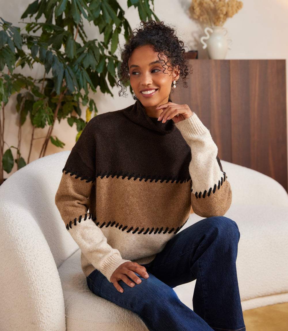 Woman wearing petite size colorblock sweater with contrast stitch mock neck and drop shoulders sitting on white sofa