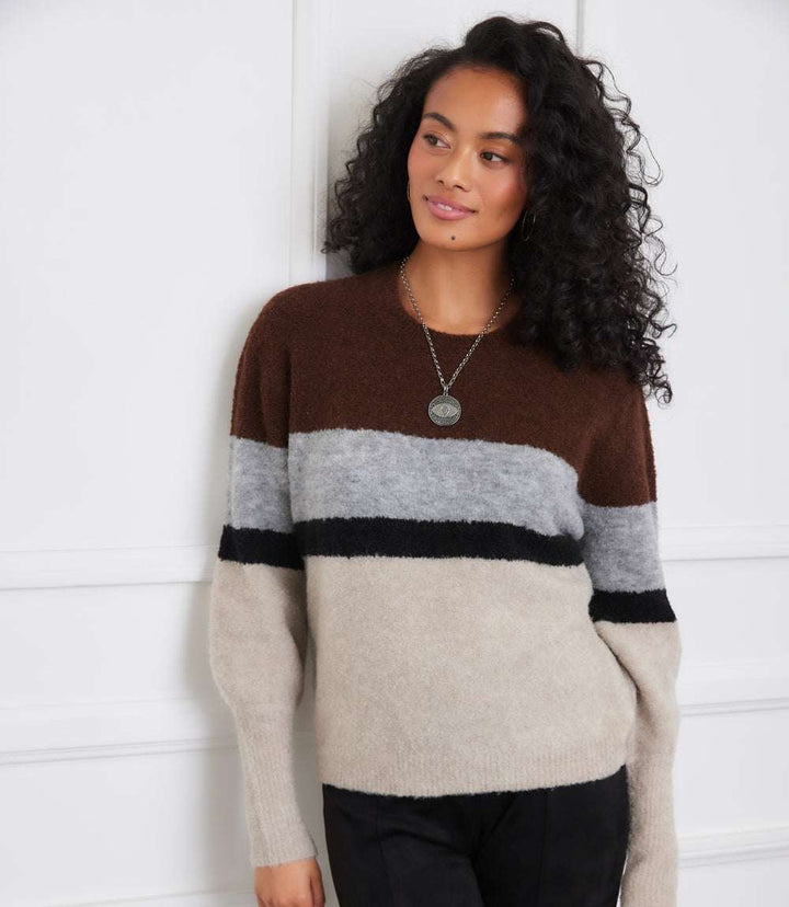 Woman wearing colorblock crewneck sweater with brown, gray, black, and oatmeal stripes and long sleeves