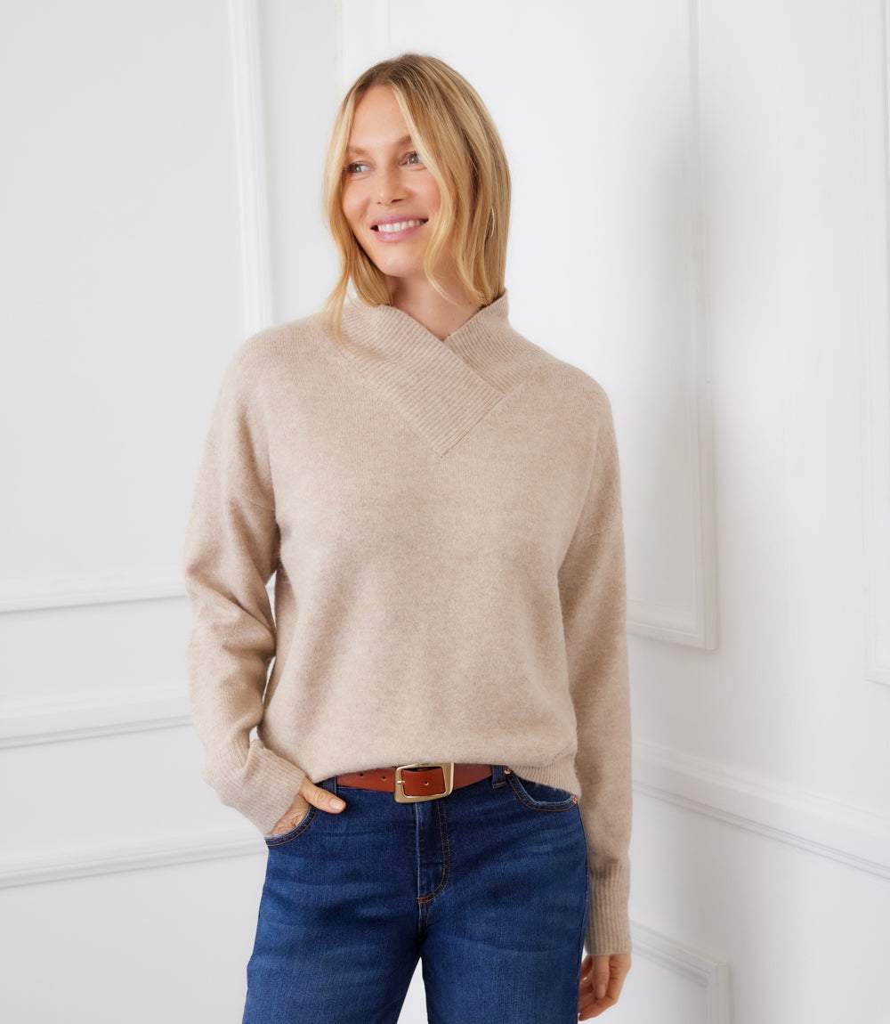 Woman wearing a beige shawl collar sweater with drop shoulders and ribbed cuffs, paired with blue jeans.