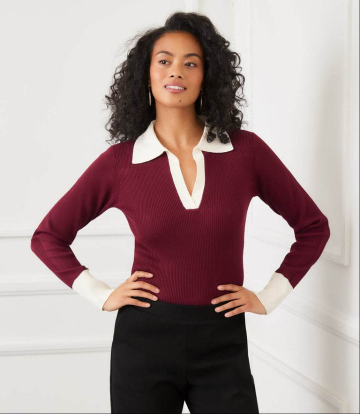 Woman wearing a burgundy contrast ribbed polo sweater with white collar and cuffs, paired with black pants.