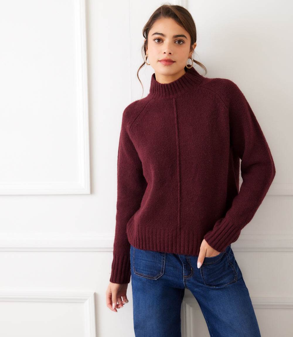 Woman wearing a burgundy turtleneck sweater with raglan sleeves and exposed center seam paired with blue jeans