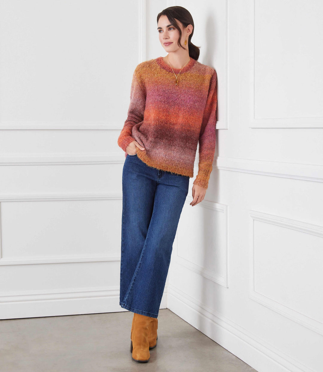 Woman wearing ombre boucle sweater with orange, pink, and brown gradient, paired with blue wide-leg jeans and brown boots.