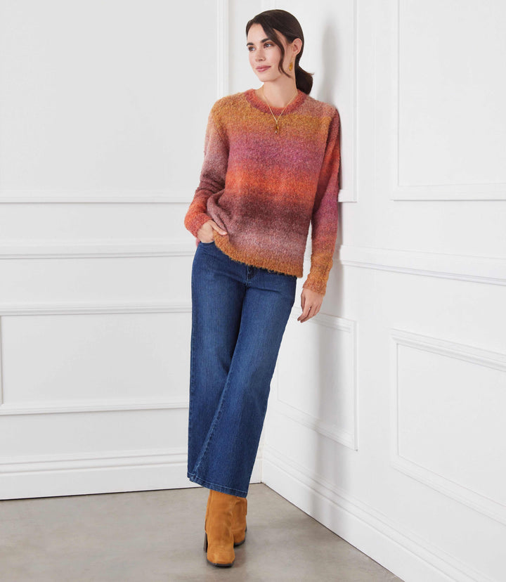 Woman wearing ombre boucle sweater with orange, pink, and brown gradient, paired with blue wide-leg jeans and brown boots.