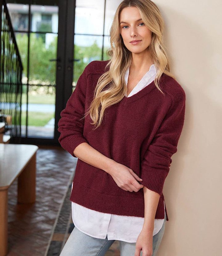Petite size layered sweater with V-neck, raglan sleeves, and shirt collar detail in burgundy with faux-layered shirttail hem.