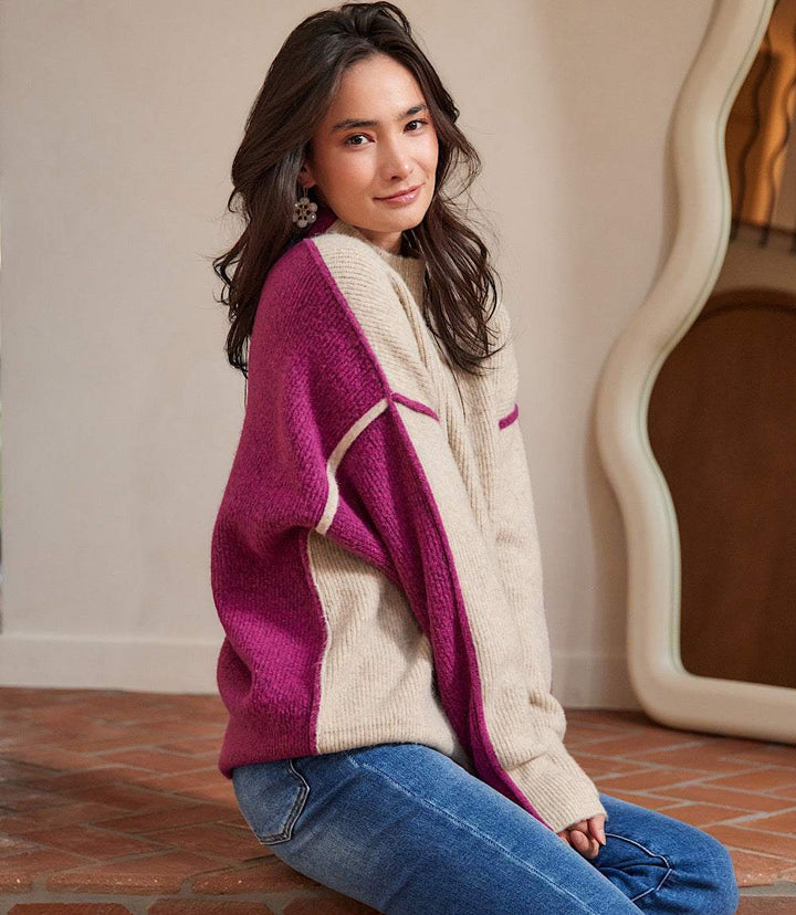 woman wearing beige and magenta colorblock mock neck sweater with drop shoulder sleeves sitting on floor