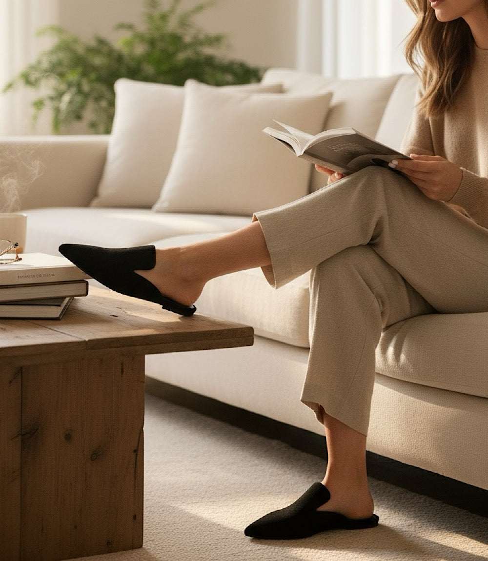 Black suede leather mules on woman's feet with flat sole, styled for comfort and elegance indoors