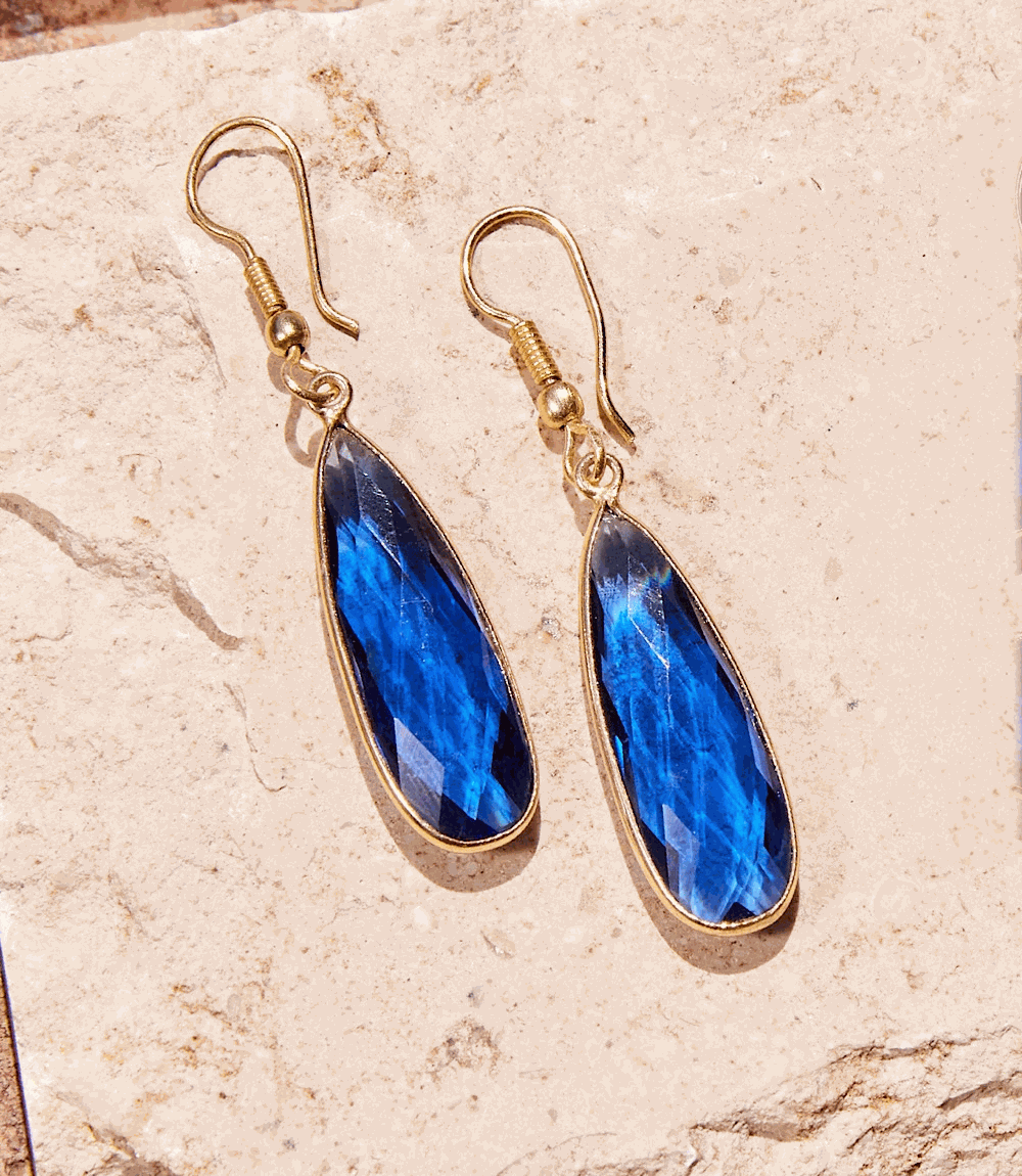 Pair of gold-tone dangle blue quartz earrings with faceted teardrop stones on natural stone background
