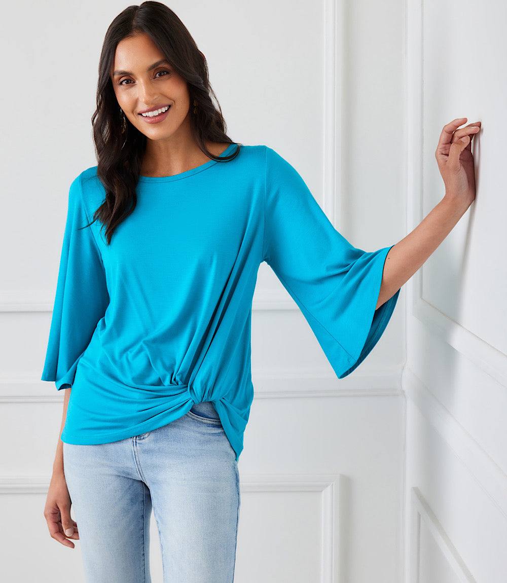 Woman wearing a blue Flare Sleeve Pick-Up Top with boat neck and twist hem paired with light jeans.