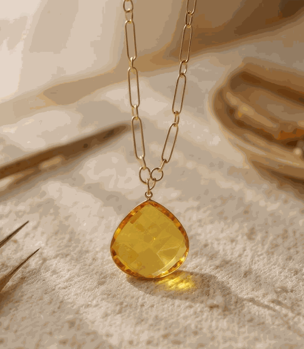 Faceted citrine quartz pendant with gold plated brass chain on a soft surface