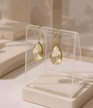 Pear drop gemstone earrings with lemon yellow topaz and gold plating displayed on clear stand