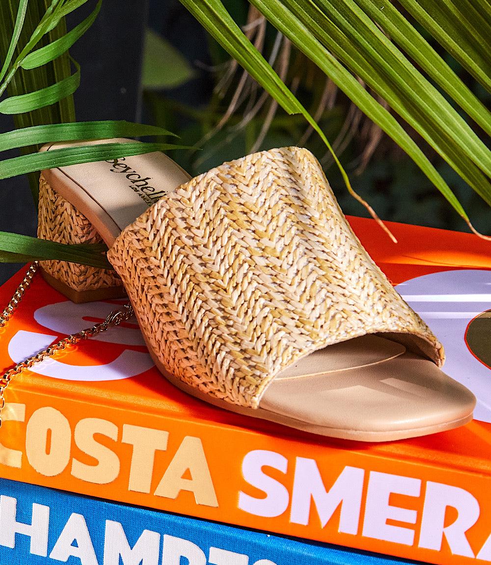 Pepper Mid Heel Sandals with natural raffia wide strap and 1.75-inch block heel on colorful books background