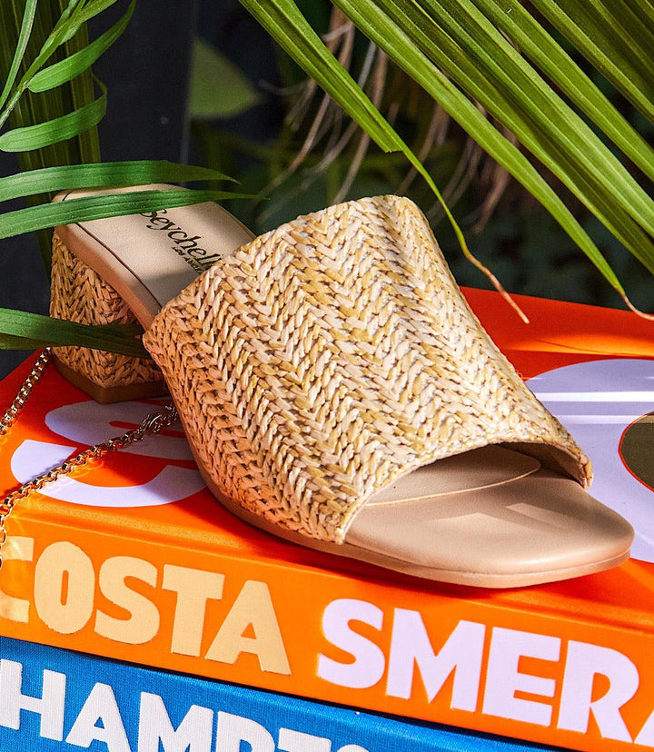 Pepper Mid Heel Sandals with natural raffia wide strap and 1.75-inch block heel on colorful books background