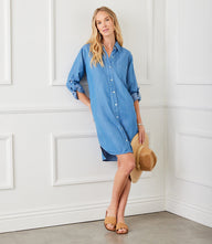 Woman wearing Roll Tab Chambray Shirtdress in blue with front buttons, collar, patch pocket, and roll-tab sleeves, holding a hat.