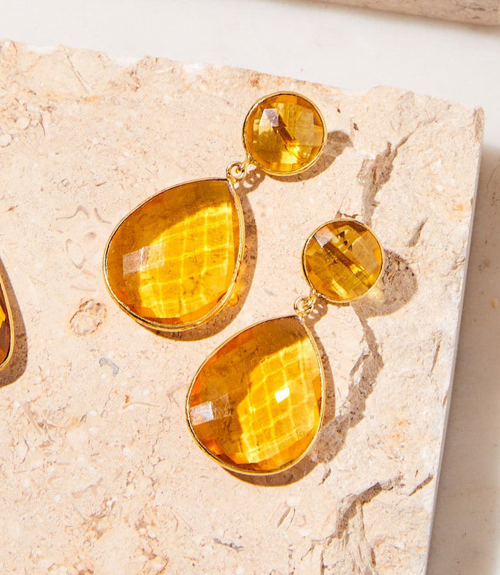 Teardrop gemstone citrine drop earrings with gold plating on a textured stone surface