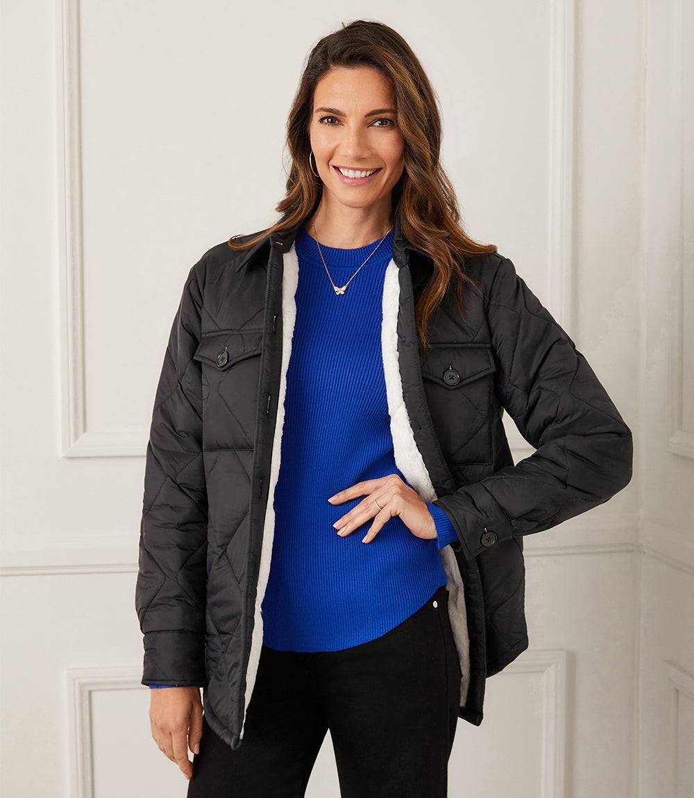 Woman wearing black faux fur quilted jacket with collar, front button closure, and side pockets over blue sweater