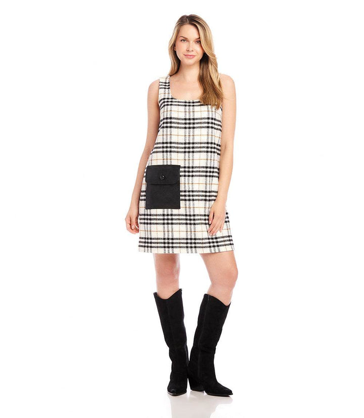 Woman wearing sleeveless plaid shift dress with faux leather patch pocket and black boots