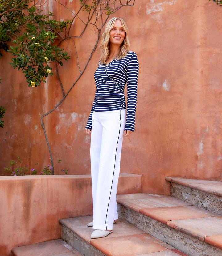 Woman wearing navy and white long sleeve stripe crossover top with white pants outdoors on steps