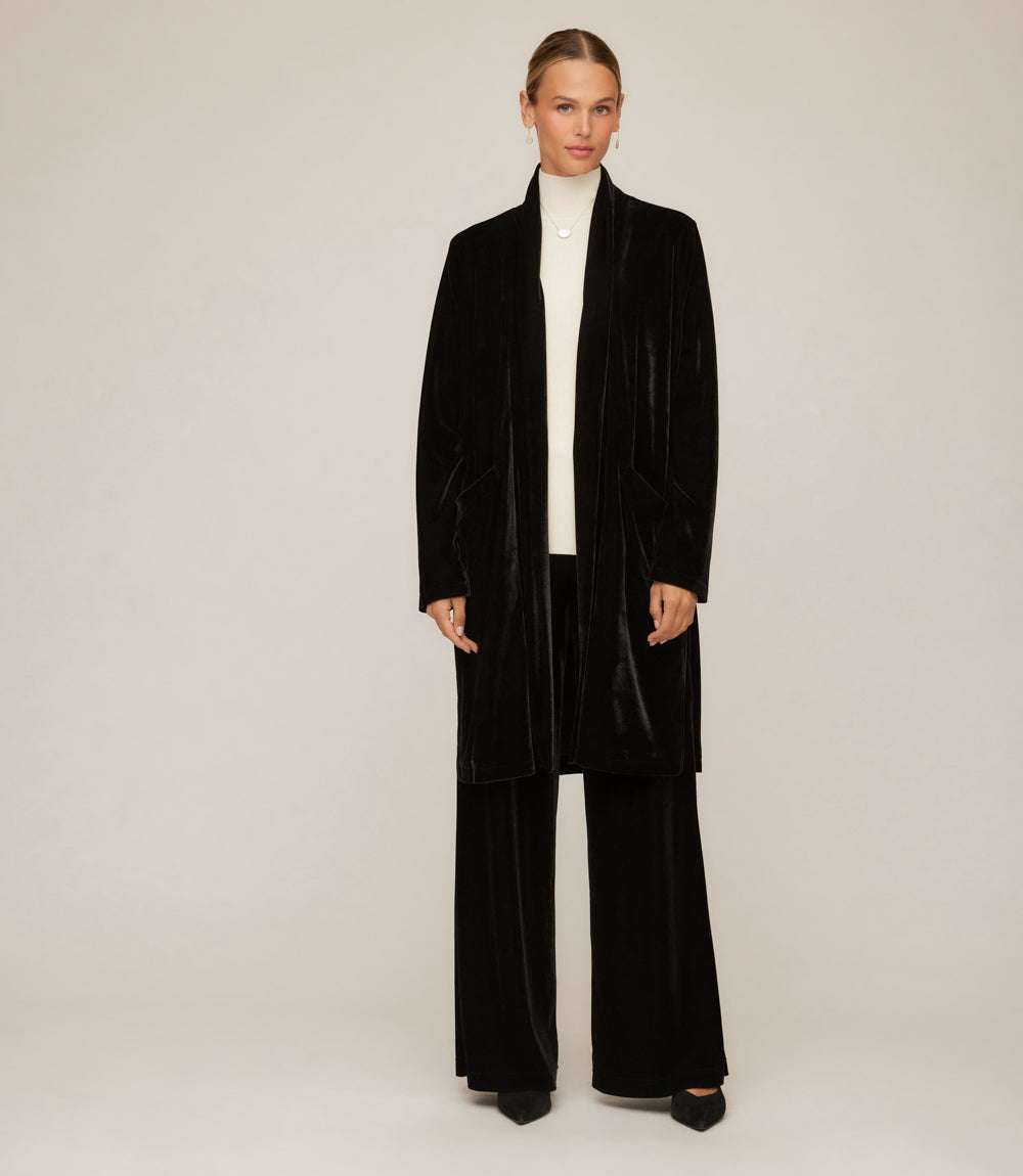 Woman wearing black velvet wide-leg pants with matching long coat and white turtleneck top