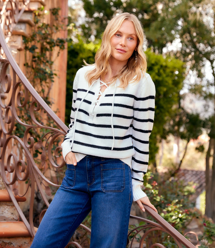 Woman wearing off white and black stripe lace-up sweater with long sleeves and tie neck detail