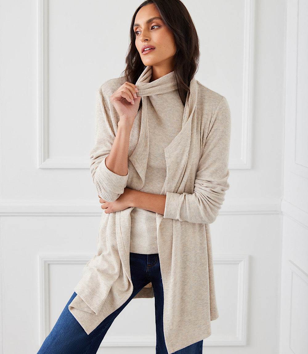 Woman wearing beige ribbed drape front cardigan with long sleeves and open front over a matching top and blue jeans.