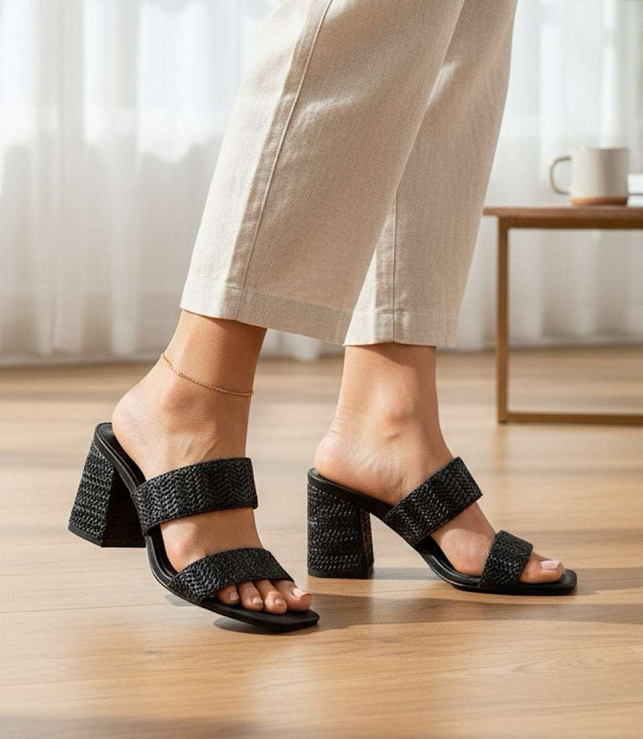 Newport Raffia Strap heel sandals with block heel and raffia upper in black worn with beige pants indoors