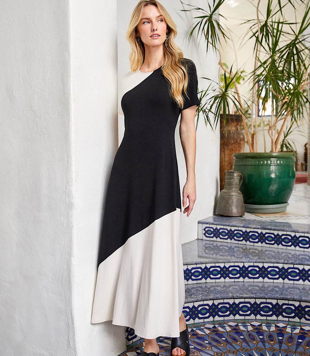 Woman wearing short sleeve contrast midi dress with black and ecru colorblock panels standing indoors near tiled stairs.