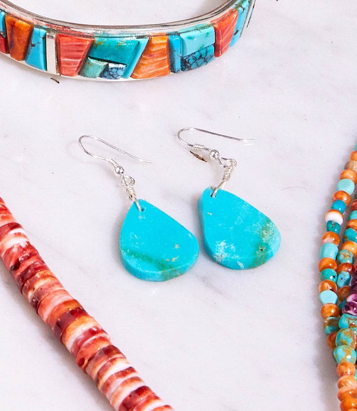 Turquoise stone drop earrings with sterling silver hooks, unique natural variations, displayed with colorful beaded jewelry.