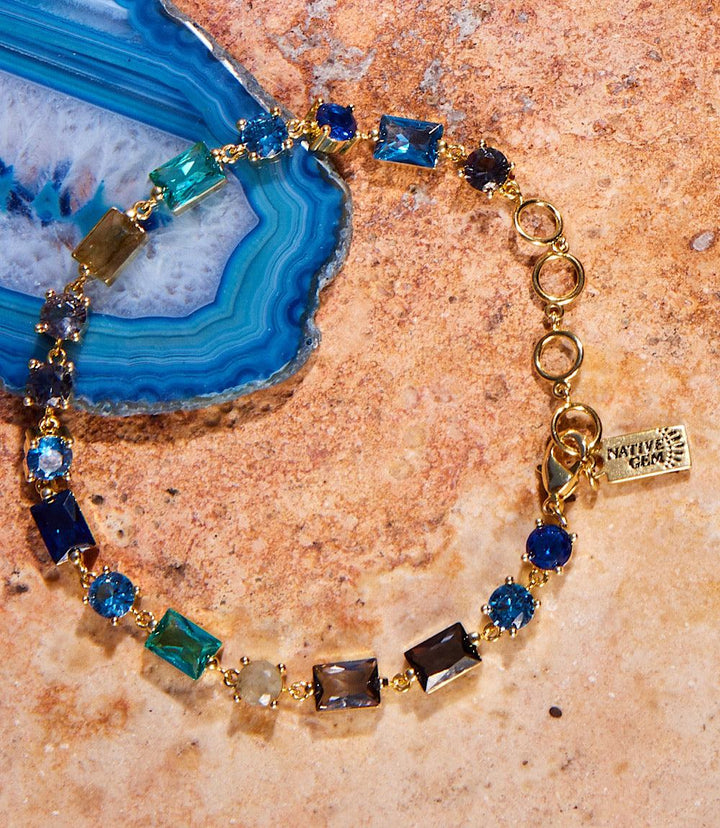 Atlantis Crystal Bracelet with multi color cubic zirconia and 14k gold vermeil on a stone background