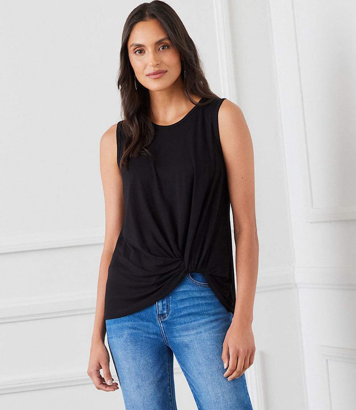 Woman wearing black sleeveless pick-up top with twist hem and crew neck paired with blue jeans in bright indoor setting