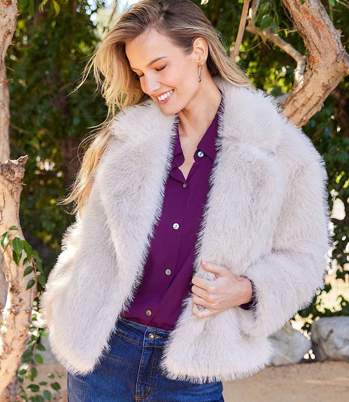 Woman wearing a cropped faux fur jacket with long sleeves and wide notched collar over a purple button-front shirt outdoors