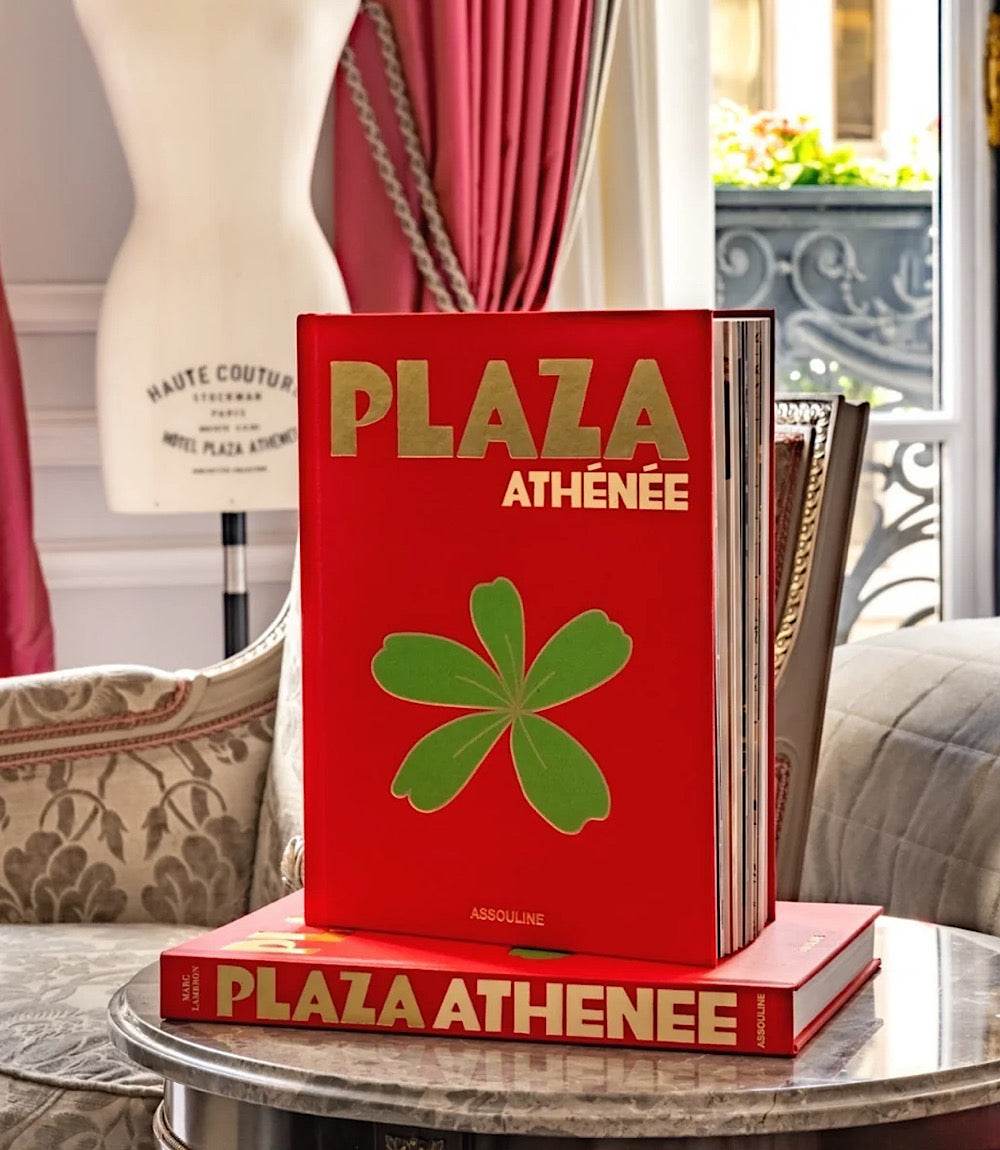 Hardcover Plaza Athénée book with red cover and green clover design on a marble table in elegant room