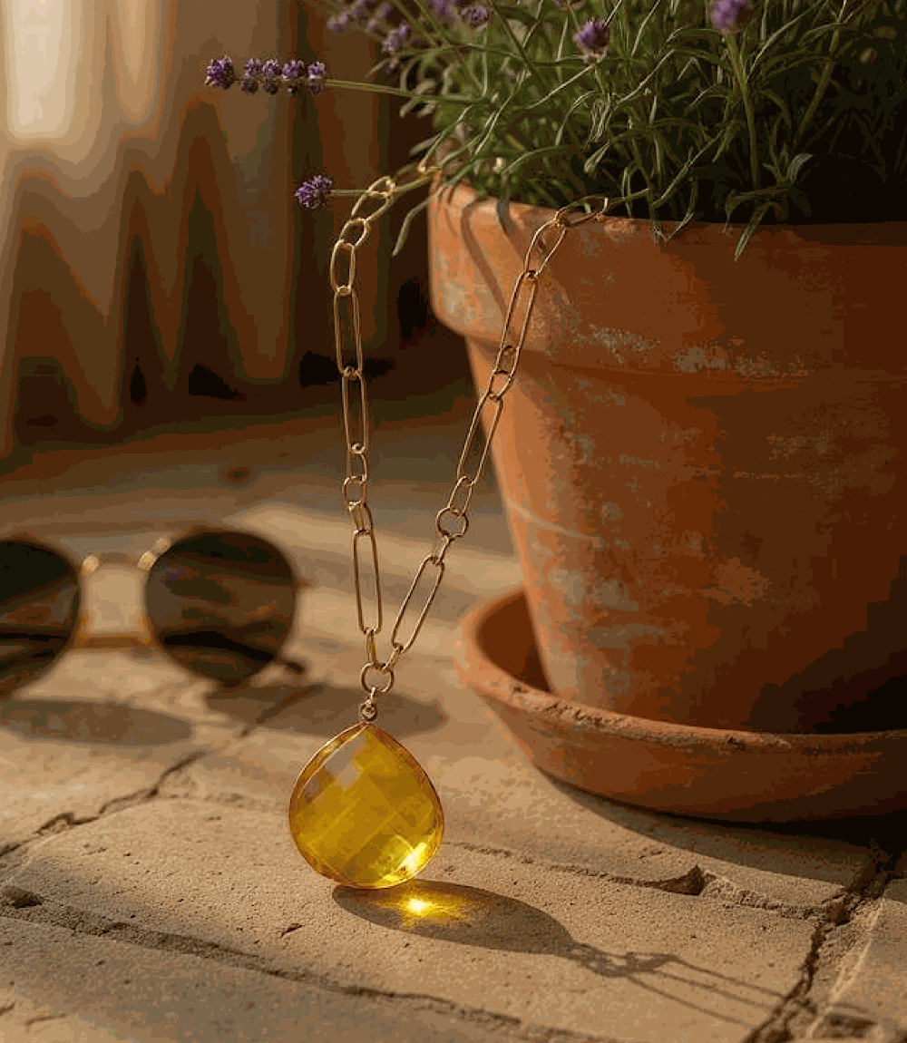 Faceted citrine quartz pendant necklace with gold-plated chain displayed near terracotta pot and sunglasses