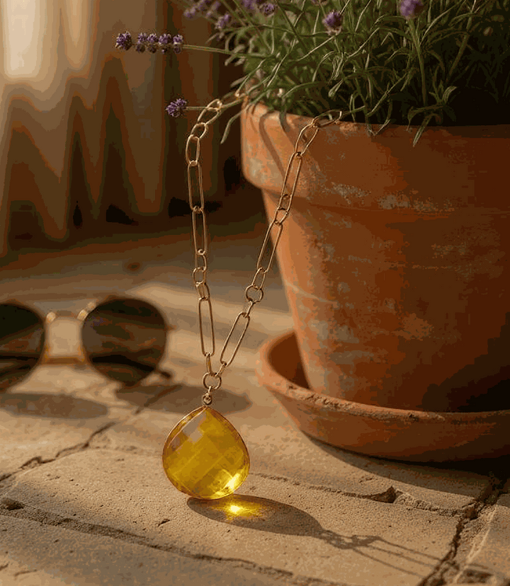 Faceted citrine quartz pendant necklace with gold-plated chain displayed near terracotta pot and sunglasses
