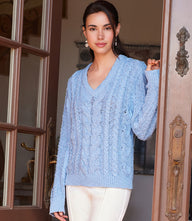 Woman wearing light blue cable knit sweater with V-neck and long sleeves standing by doorway