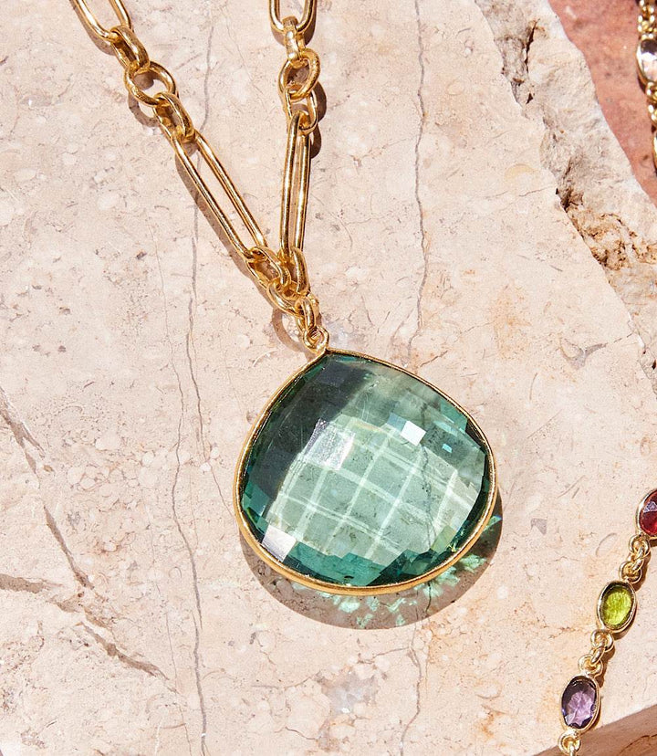 Aqua quartz pendant necklace with gold chain on stone background