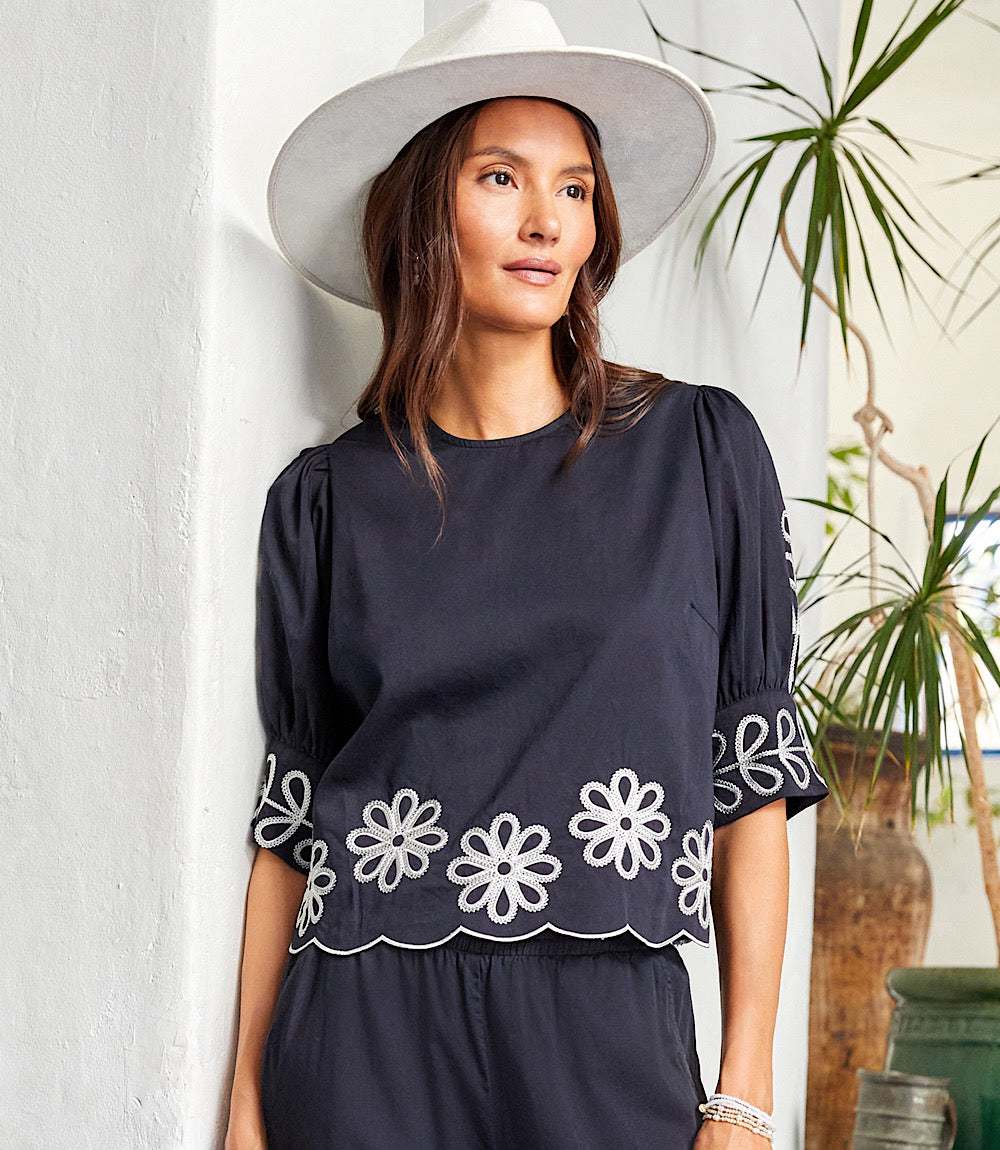 Woman wearing a black 3/4 sleeve embroidered scallop top with floral embroidery and puff sleeves