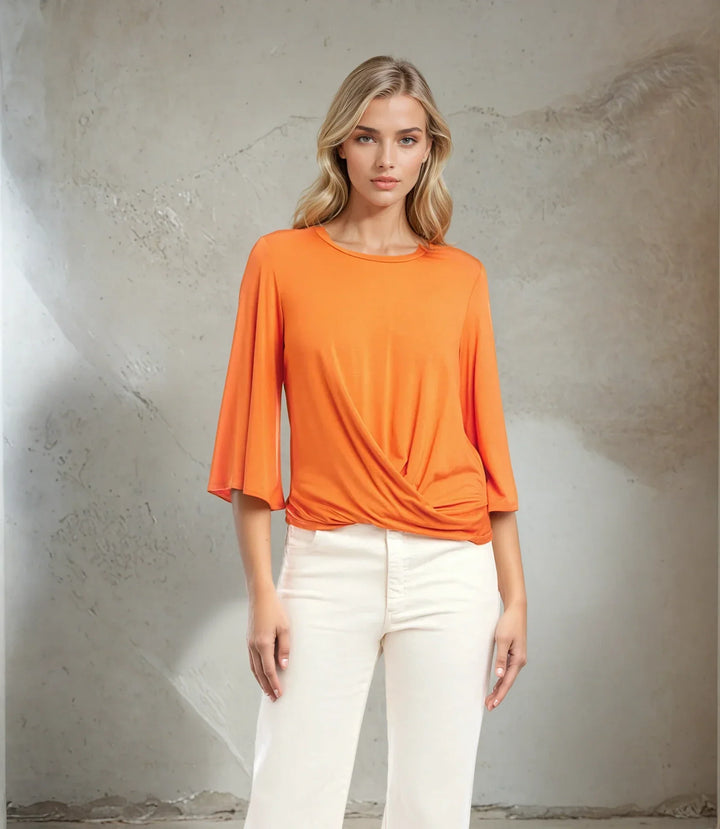 Woman wearing orange drape front top with bell sleeves and twist front seam paired with white pants
