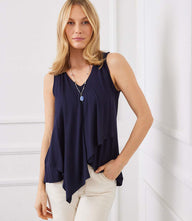 Woman wearing navy sleeveless drape front tank top with V-neck and asymmetrical hem paired with light pants