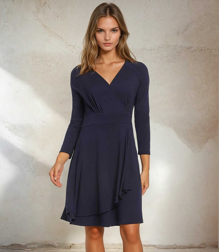 Woman wearing a navy Faux Wrap Drape Dress with 3/4 sleeves and surplice neckline standing against a neutral background