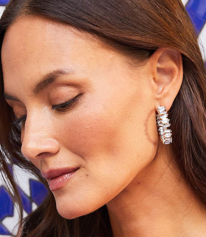 Close-up of a woman wearing angled crystal hoop earrings with clear crystals and 14k gold detailing.