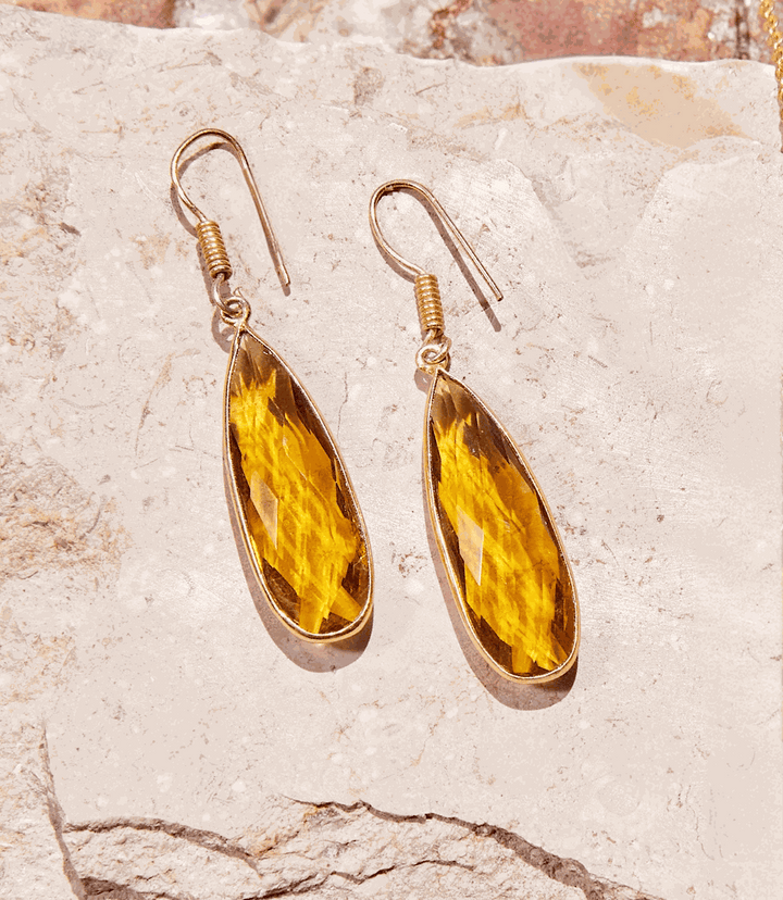 Gold plated Citrine quartz drop earrings with vibrant yellow stones on beige stone background