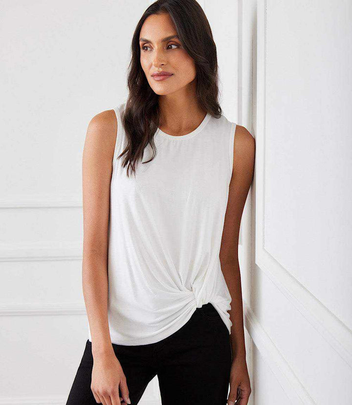 Woman wearing white sleeveless pick-up top with twist hem and crew neck paired with black pants.