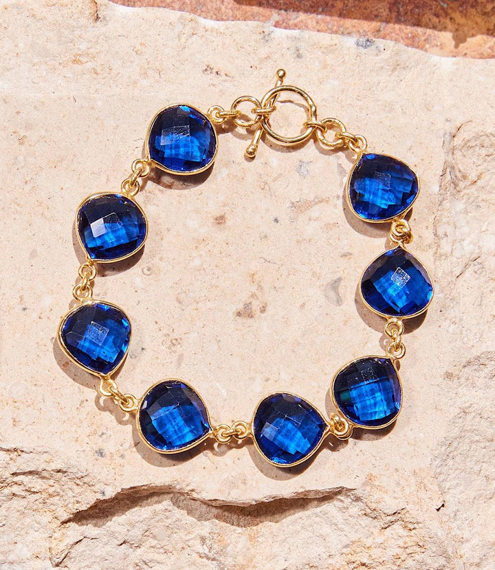 Blue quartz bracelet with gold settings and toggle clasp on a textured stone background