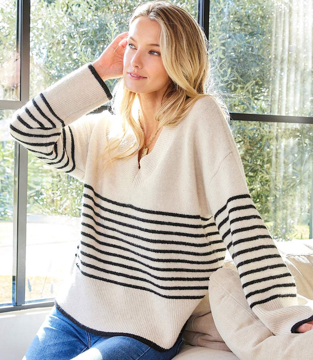 Woman wearing a relaxed fit stripe V-neck sweater with drop shoulder long sleeves and black horizontal stripes.