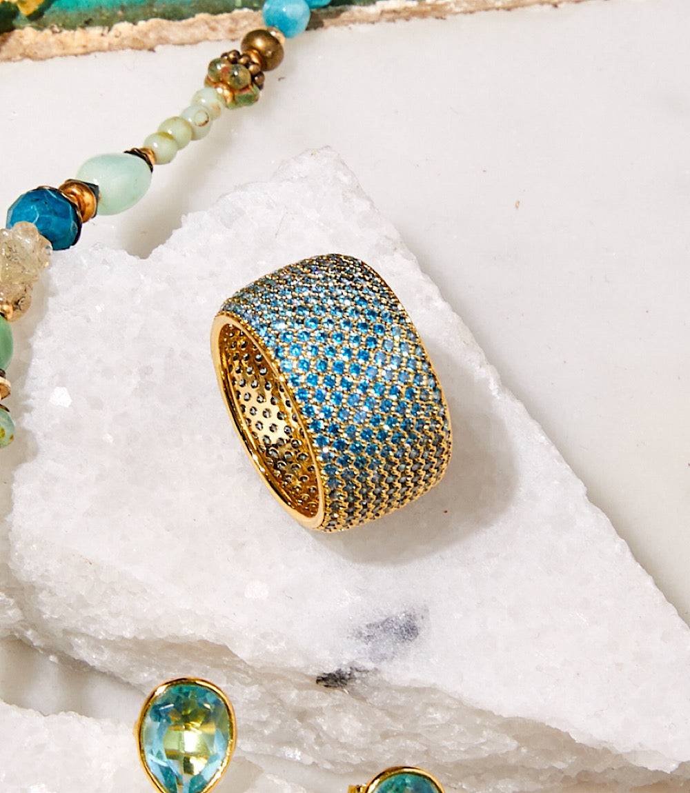 14k gold vermeil colorful crystal ring with blue cubic zirconia stones on white stone background