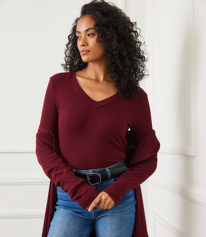 Woman wearing a petite size long sleeve ribbed V-neck top in burgundy